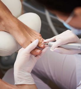 Pedicurist using electric nail drill while doing pedicure for young lady